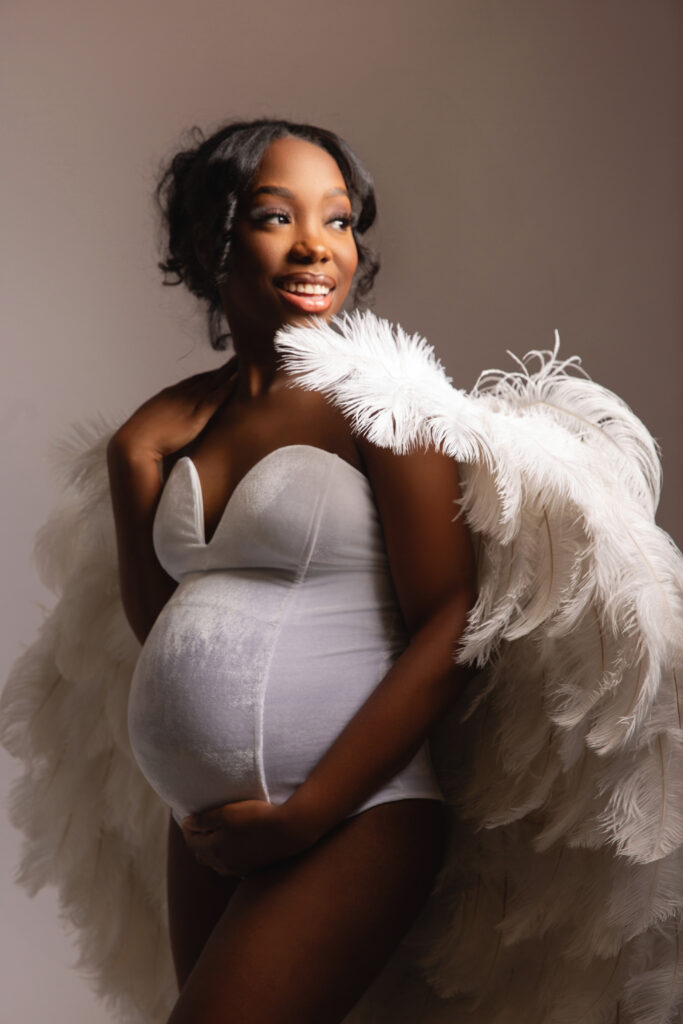 Mother posing alone in angels wings for maternity shoot with baby bump in velvet body suit.